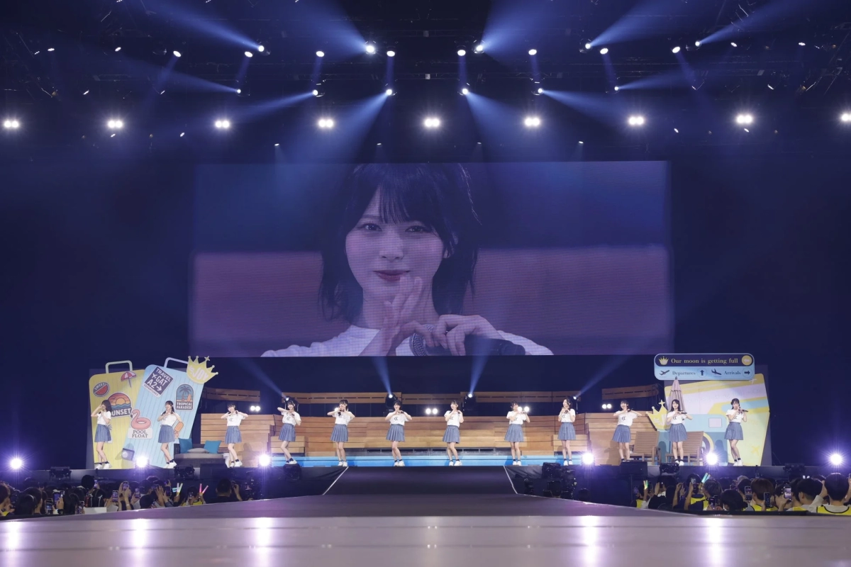 ≒JOY members on stage with a large screen displaying travel themes