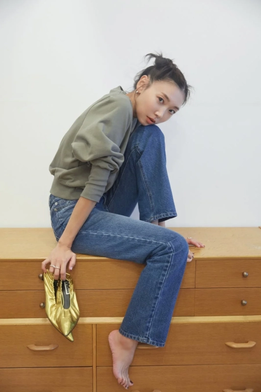 Woman in sweat and denim, holding gold shoes