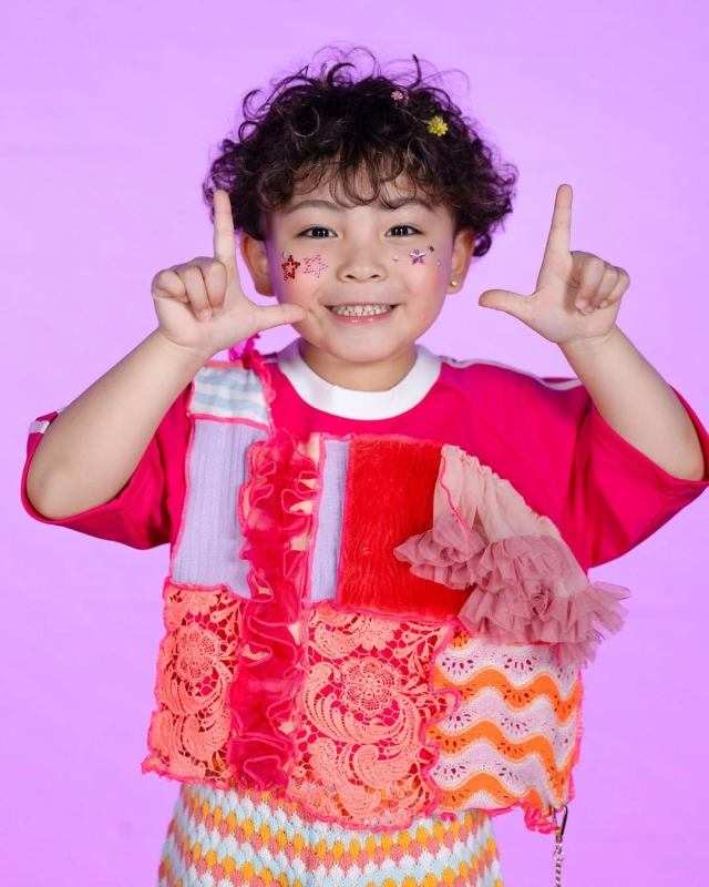 Rio, a child with curly hair, smiling in a colorful patchwork-style outfit