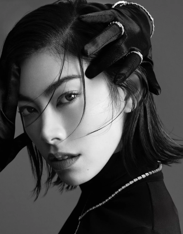 A monochrome close-up portrait of Hikari Mori, wearing a turtleneck and gloves, with her hair flowing across her face