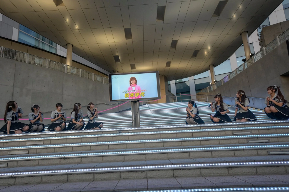 Idol group on stage with Iyo Matsumoto on a large screen