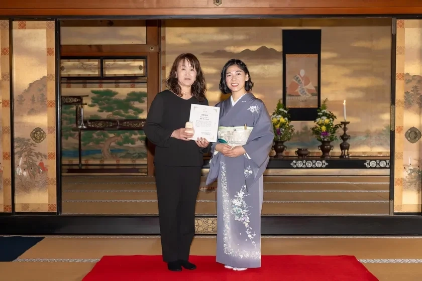 Two women, one holding a certificate, in a traditional Japanese room.