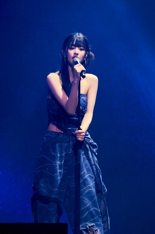 Female singer performing on stage with a microphone, wearing a denim outfit