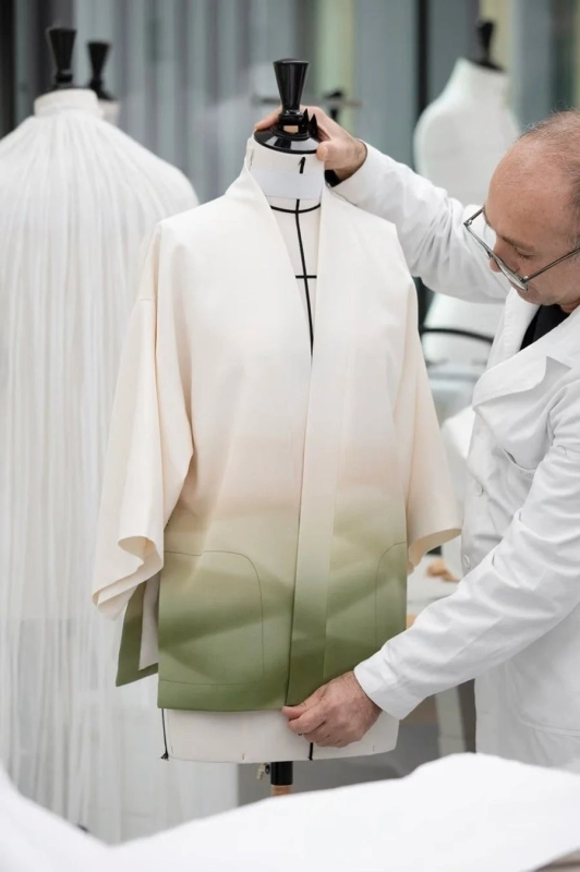 A designer adjusting a white kimono-style garment with a gradient on a mannequin in a studio setting