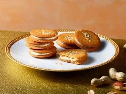 Round peanut cookies with cream filling, stacked on a white plate, with some shelled peanuts scattered around.