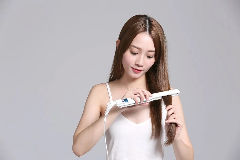 A woman using a white hair iron on her long hair.