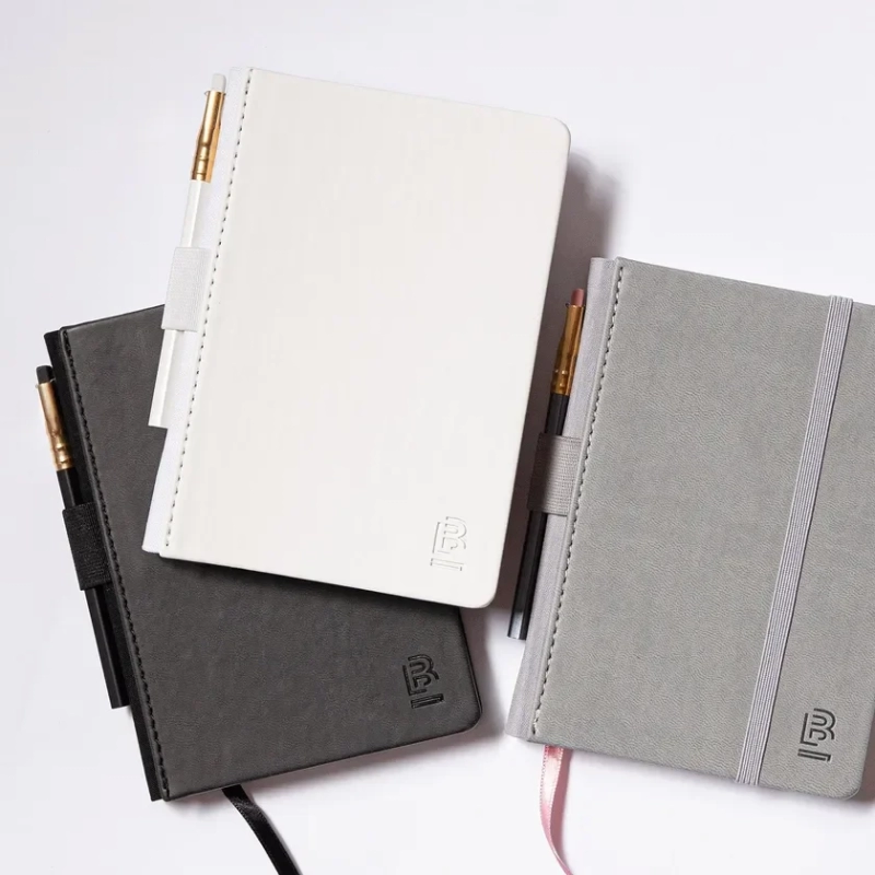 Blackwing notebooks in white, black, and grey, with a pencil