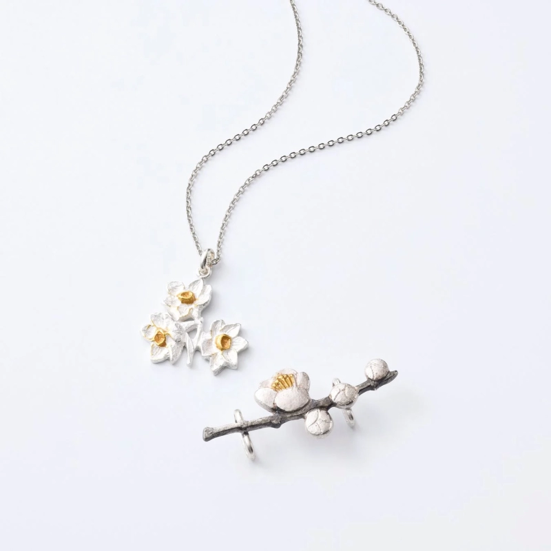 Delicate silver and gold jewelry with flower motifs, including a three-flower necklace and a plum blossom ear cuff/brooch.