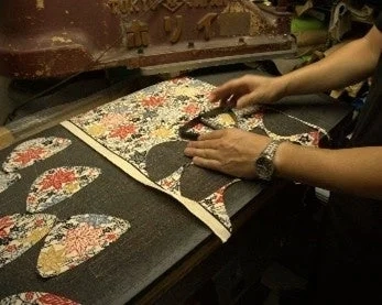 A craftsman's hands carefully cutting kimono fabric