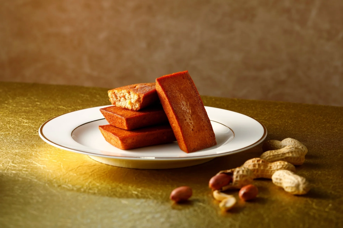 Financiers on a white plate against a golden background, with shelled peanuts on the side.