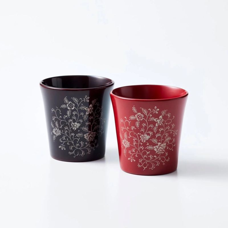A pair of traditional Wajima-nuri lacquerware cups in red and black, adorned with delicate floral patterns.