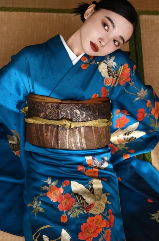 A woman in a blue kimono with floral and butterfly patterns, lying on tatami