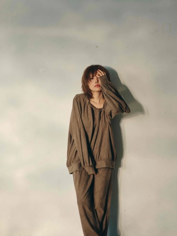 A woman with short hair wearing an oversized brown top, covering part of her face