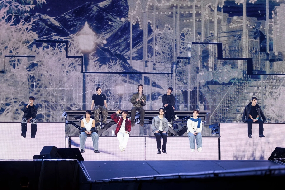 Male idol group sitting on stage with a winter scenery background on a large LED screen