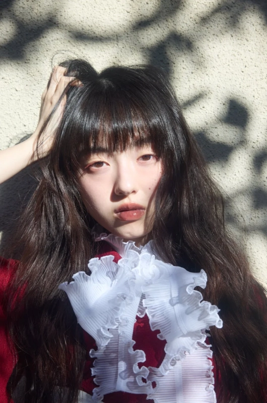 A young woman with long black hair, wearing a red top with white ruffles
