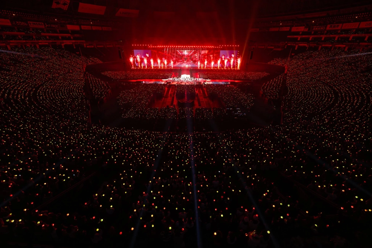 Stadium filled with an audience holding red light sticks, with fire effects on stage