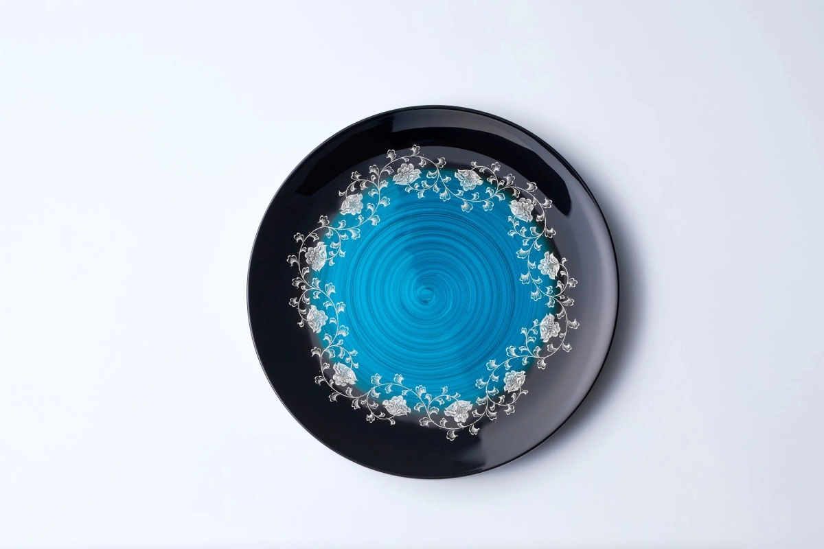 A black Wajima-nuri plate with a vibrant blue spiral center and white floral patterns around the rim.