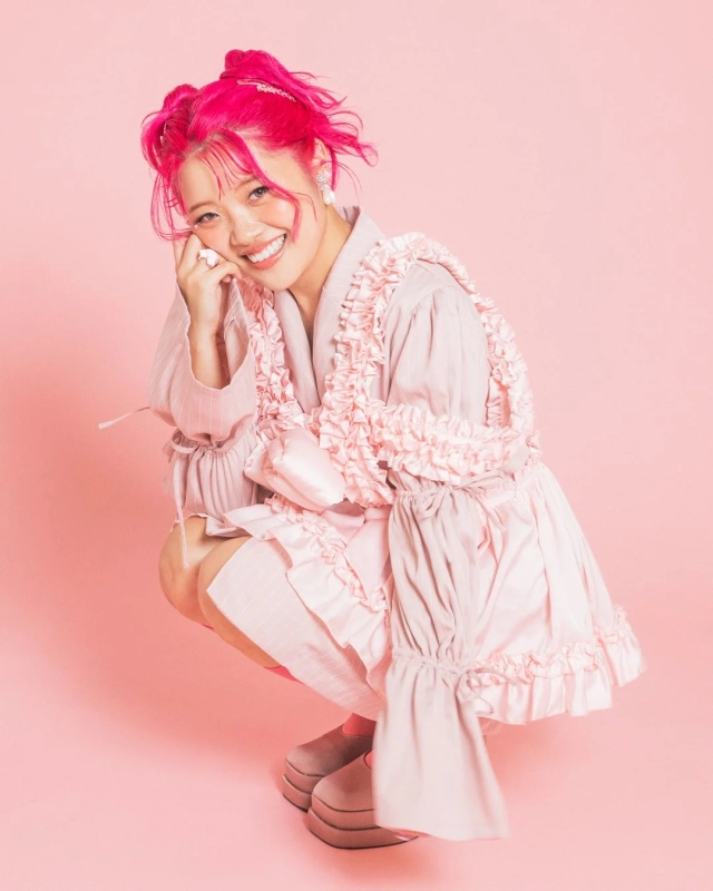 AiRI DX, a woman with vibrant pink hair, smiling in a playful pink outfit