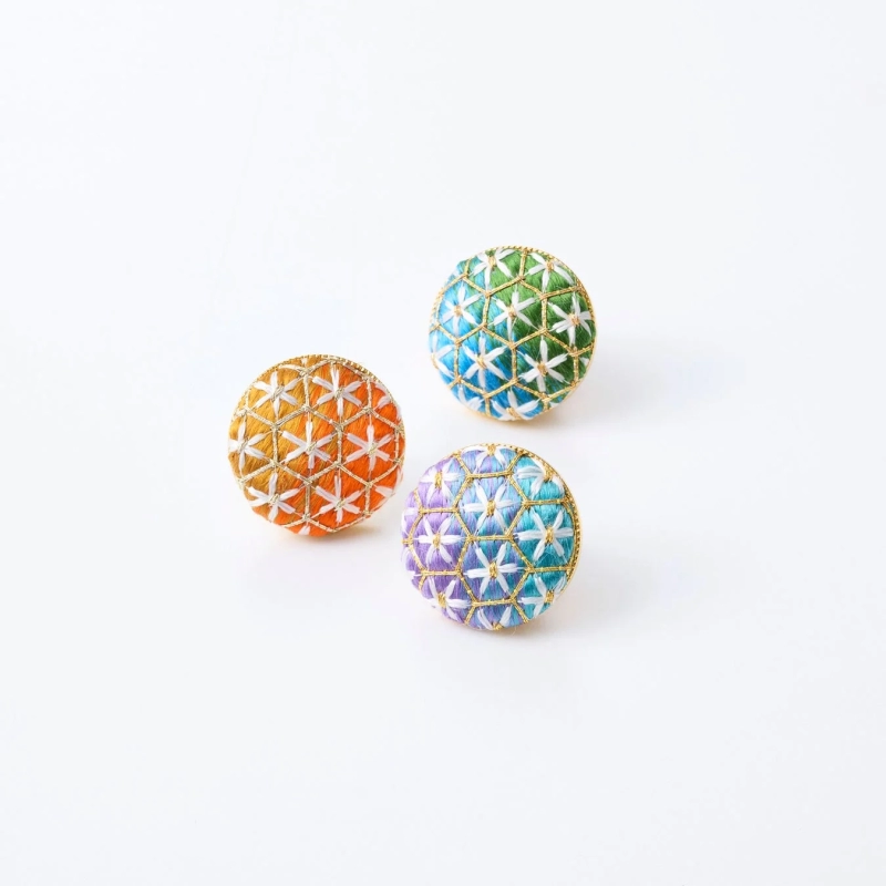 Three colorful Temari balls with intricate gold and white embroidered geometric patterns.