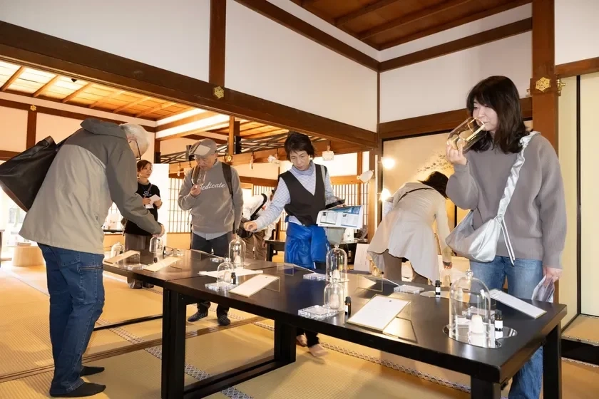 People in a Japanese room tasting fragrance samples from glasses.