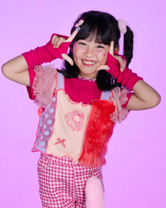 Koko, a girl in a pop and colorful outfit, smiling with glitter on her cheek