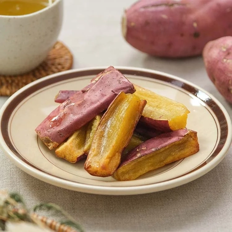 Slices of vibrant baked sweet potato are arranged on a plate with warm tea and raw sweet potatoes in the background.