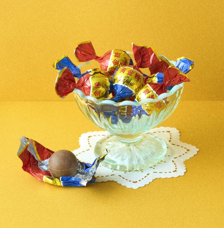 A glass bowl filled with golden-colored candies, with a single unwrapped candy beside it.