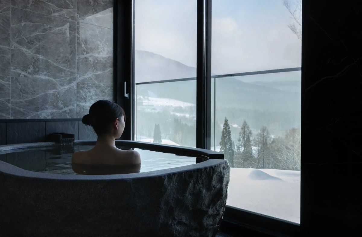 Woman relaxing in an outdoor stone bath with a snowy view