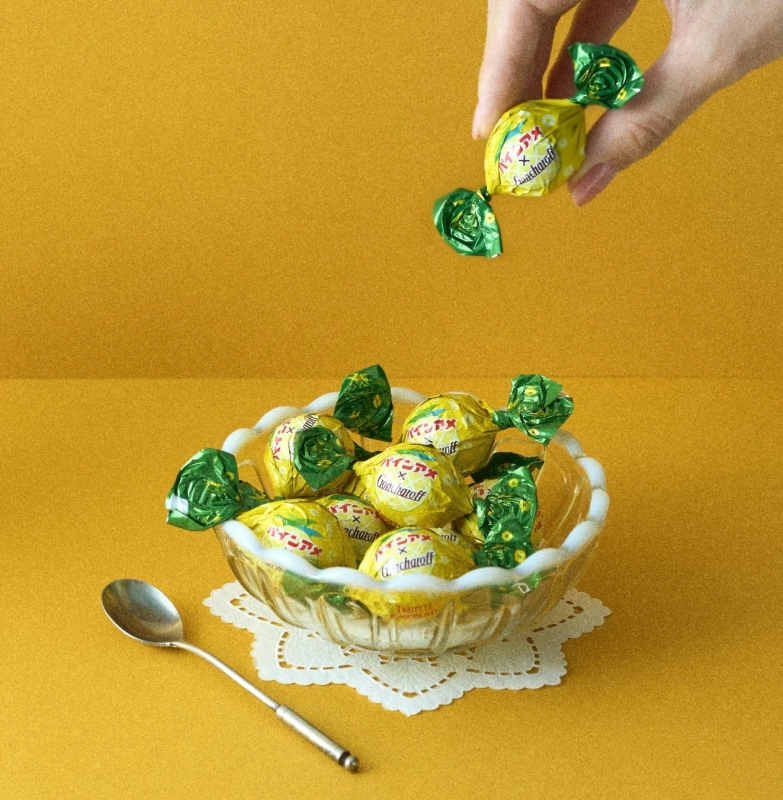 A hand dropping a candy into a glass bowl filled with candies in yellow-green wrappers.