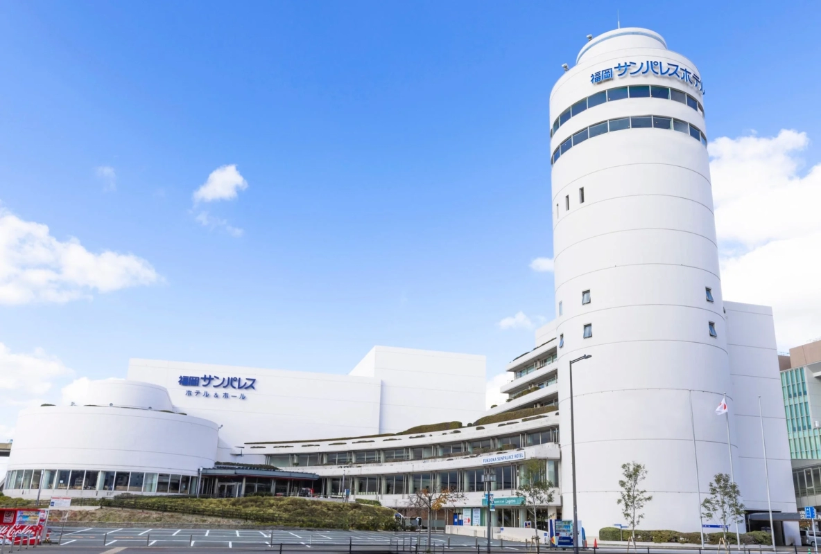 The Fukuoka Sunpalace Hotel & Hall, a modern white cylindrical building under a blue sky, serving as a prominent landmark.