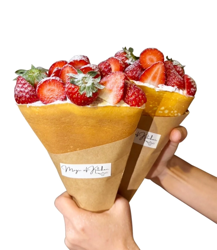 A hand holding a crepe overflowing with strawberries and whipped cream.