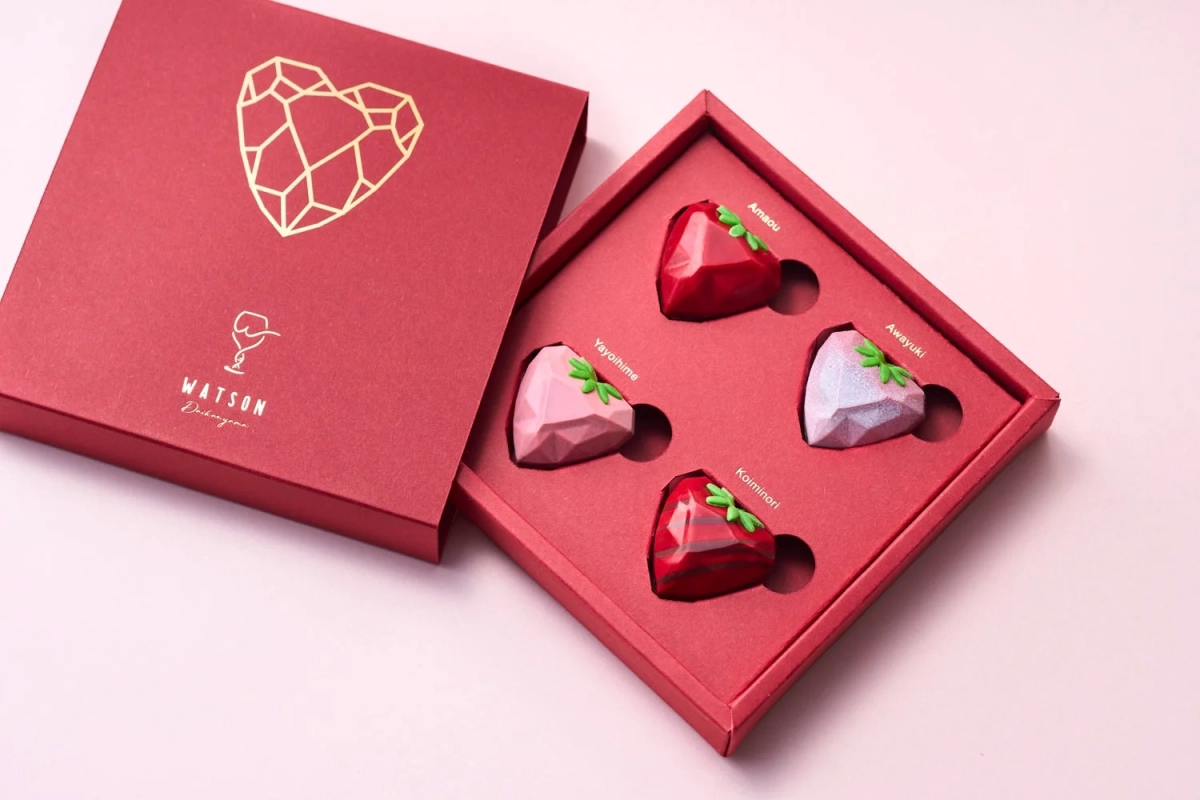A red gift box containing four heart-shaped chocolates, each representing a different type of strawberry.