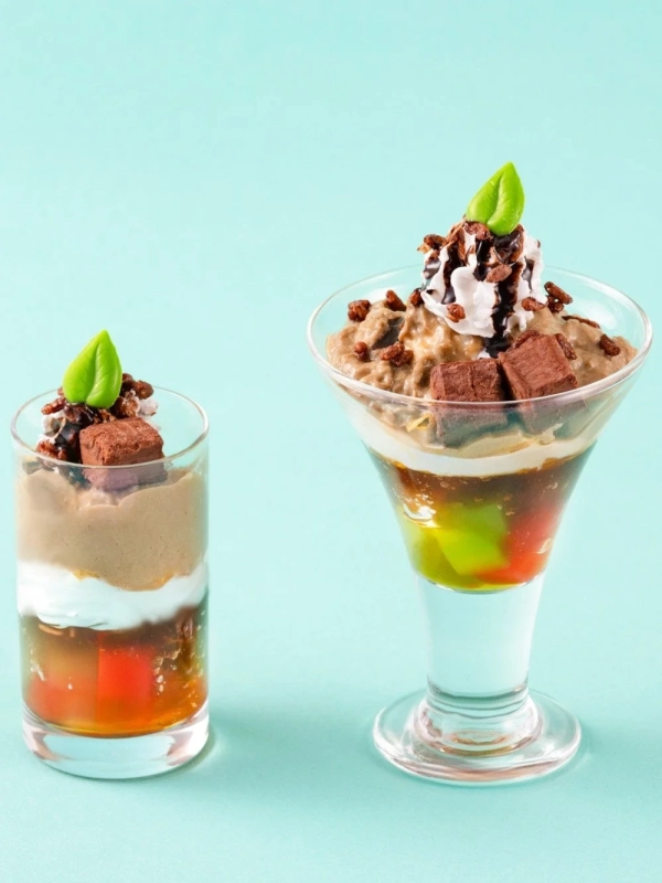 Two exquisite parfaits featuring chocolate, cream, and jelly in elegant glasses, adorned with whipped cream and mint leaves.