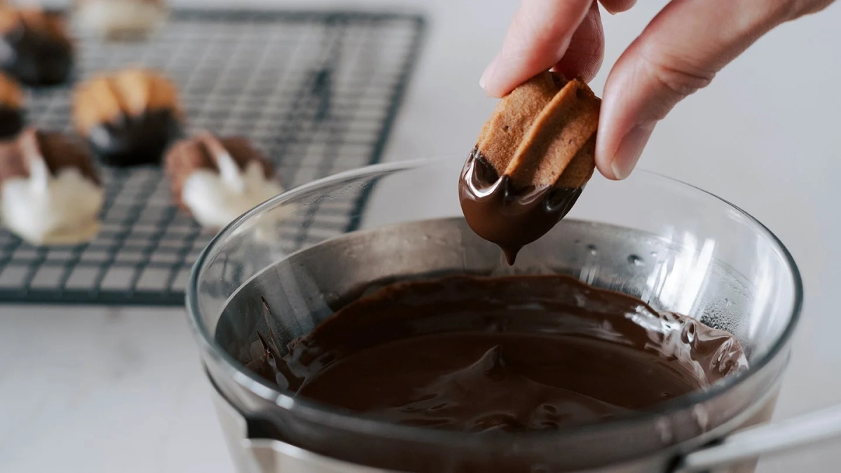Cookies being dipped into melted chocolate for coating