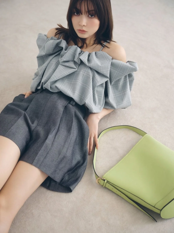 Arisa Yagi sitting in an off-shoulder checkered top and grey shorts with a lime green bag