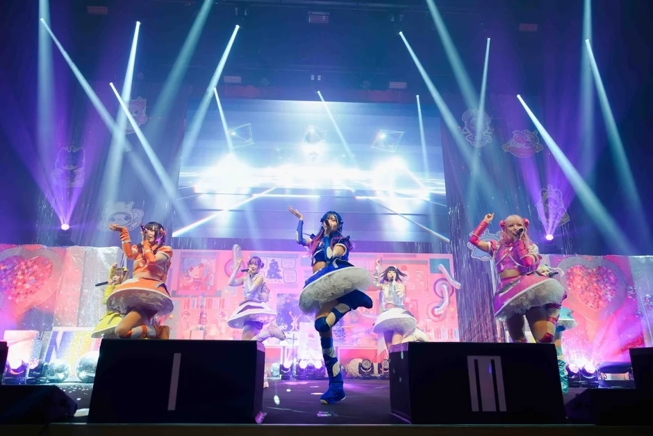 NANIMONO members in colorful costumes performing on stage under bright spotlights.