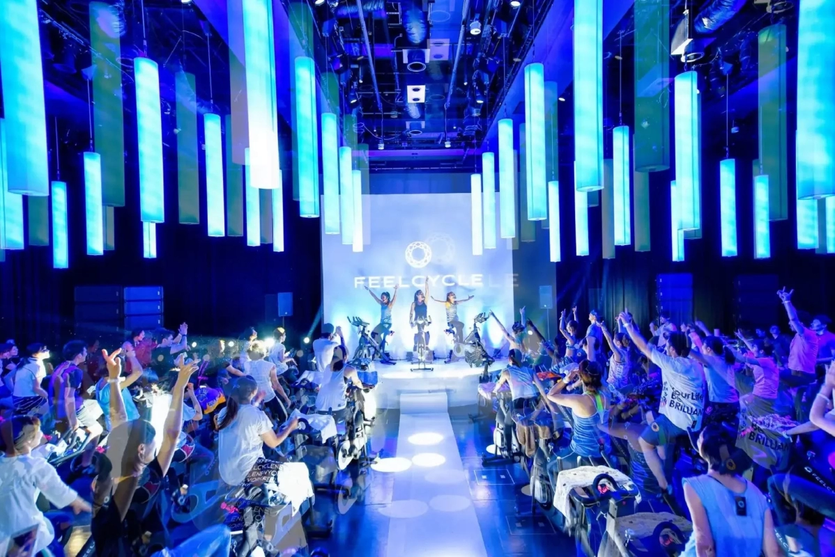 People cycling in a dark fitness studio with blue lighting and hands raised