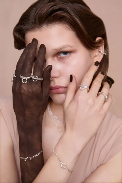 A model wearing silver jewelry, with one hand painted black covering part of her face, creating a striking contrast.