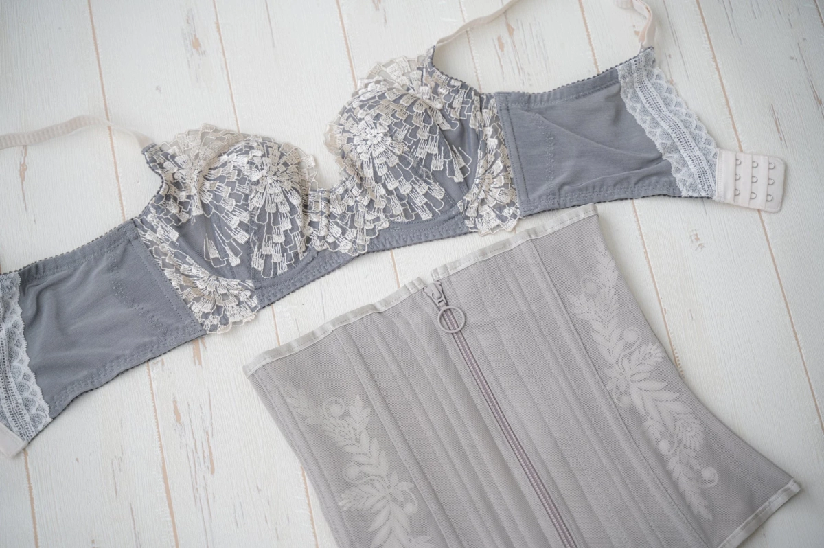 Grey lace bra and a floral embroidered waist nipper with a zipper on a white wooden background