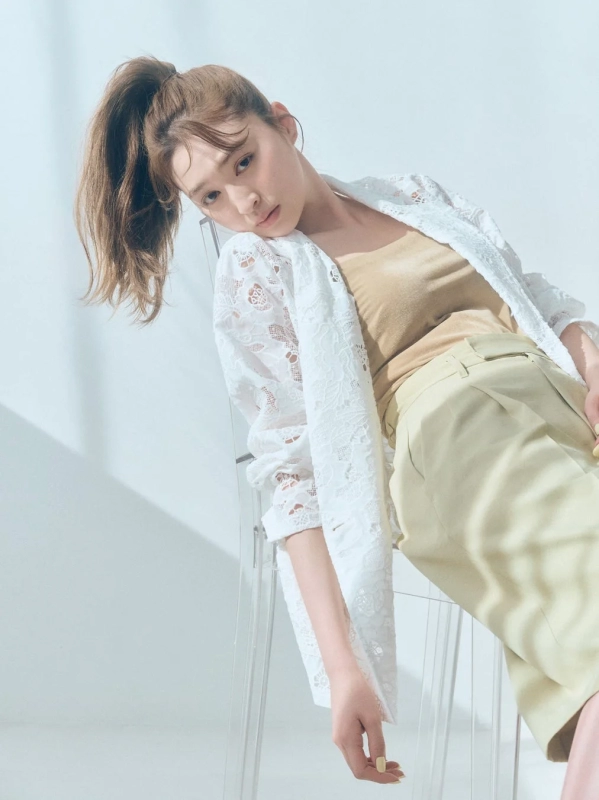A woman in a white lace shirt and beige pants, seated on a transparent chair