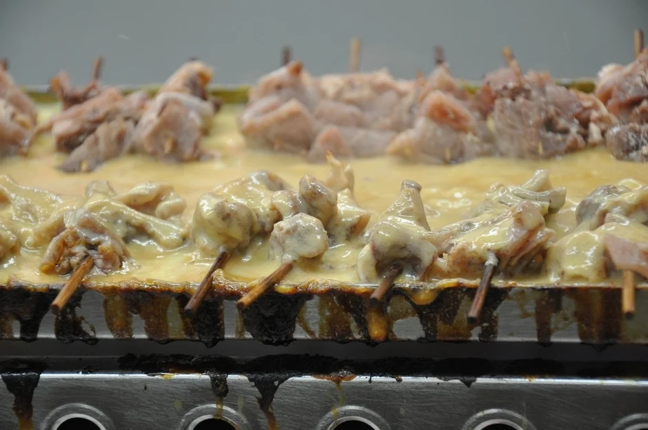 A sizzling plate of skewered meat with a rich sauce and melted cheese