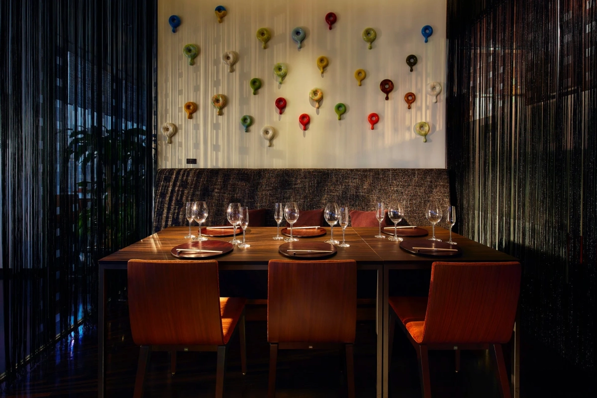 A modern and elegant restaurant dining area with beautifully set tables, wine glasses, and a distinctive art installation on the wall featuring colorful, donut-shaped objects.