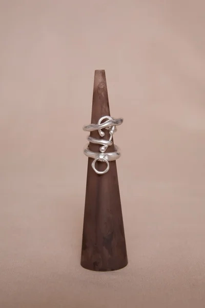 Multiple irregularly shaped silver rings are displayed on a brown conical stand, highlighting their unique designs.