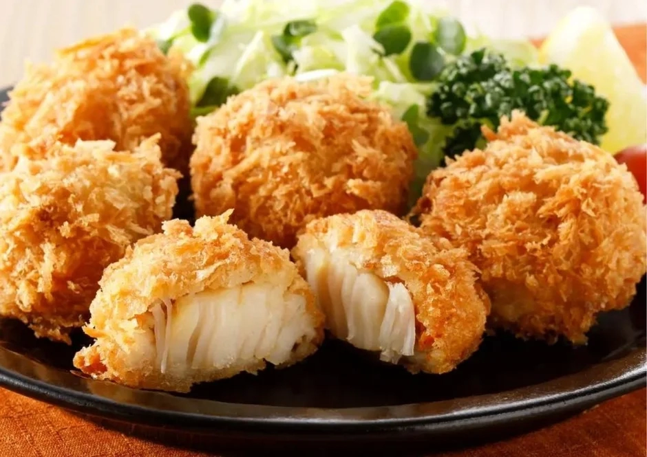 Golden-fried scallops with shredded cabbage, parsley, and a lemon wedge on a black plate