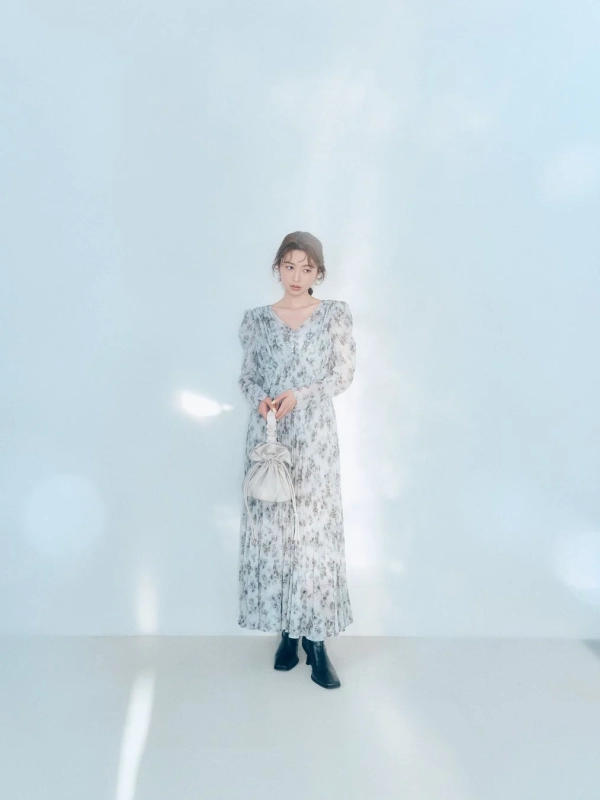 A woman in a light blue floral long dress with black boots and a handbag