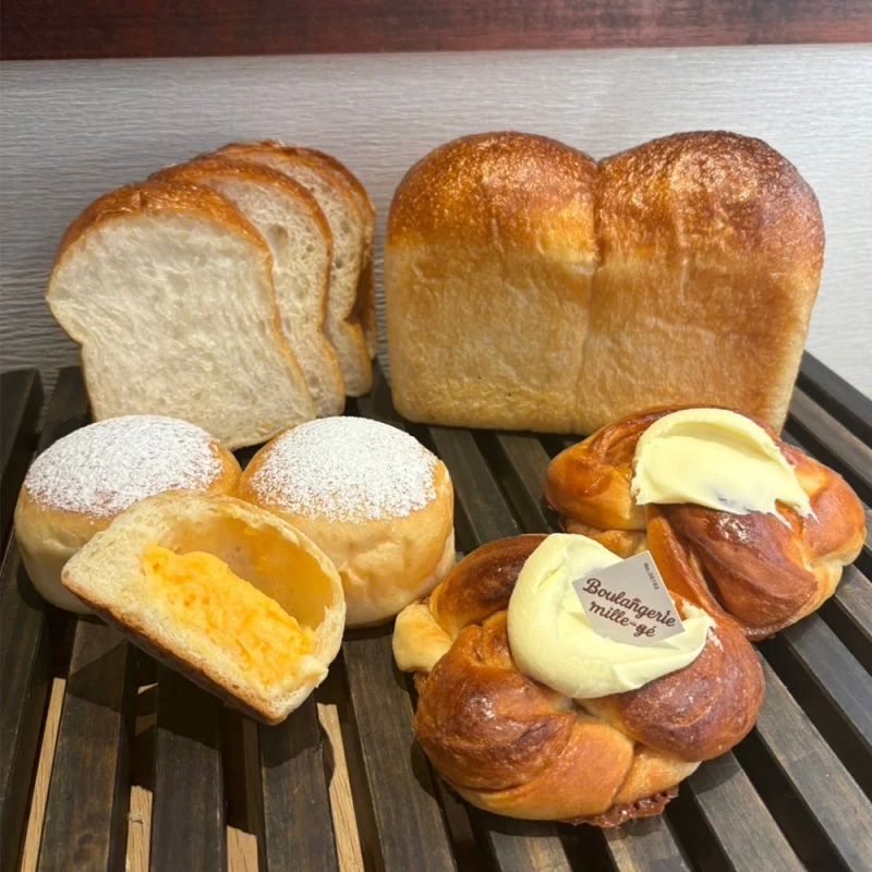 Various freshly baked breads including sliced toast, cream buns, and cinnamon rolls