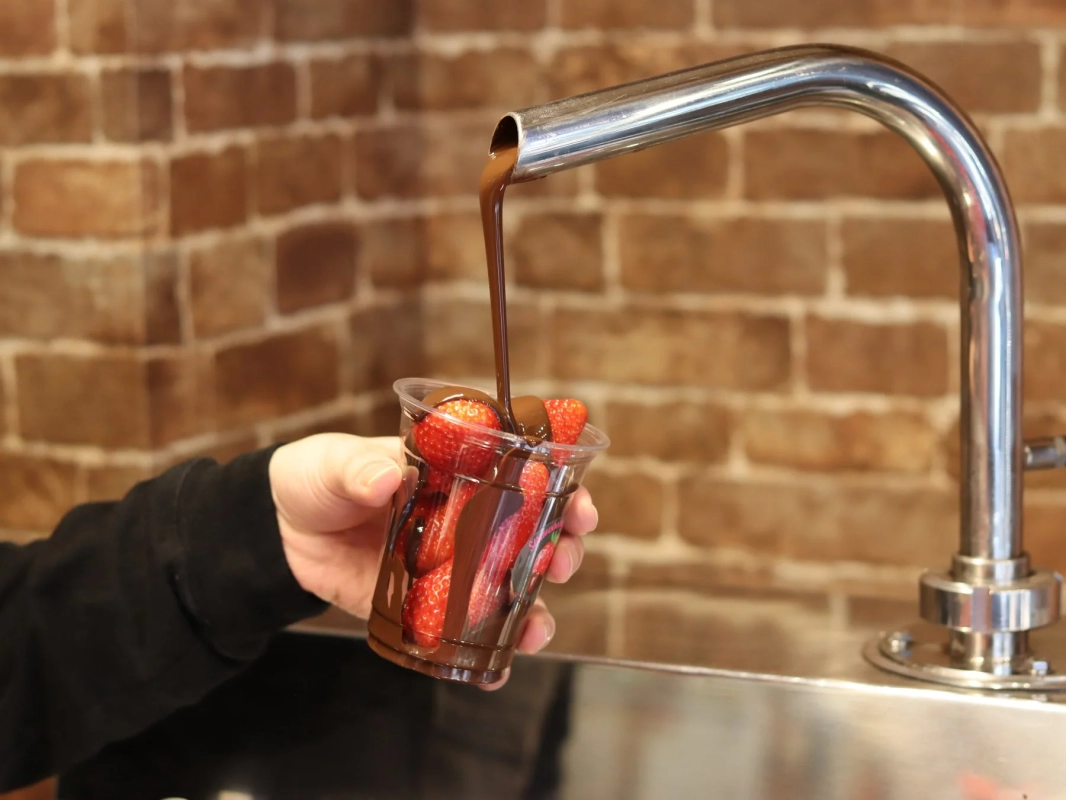Pouring melted chocolate over fresh strawberries in a cup