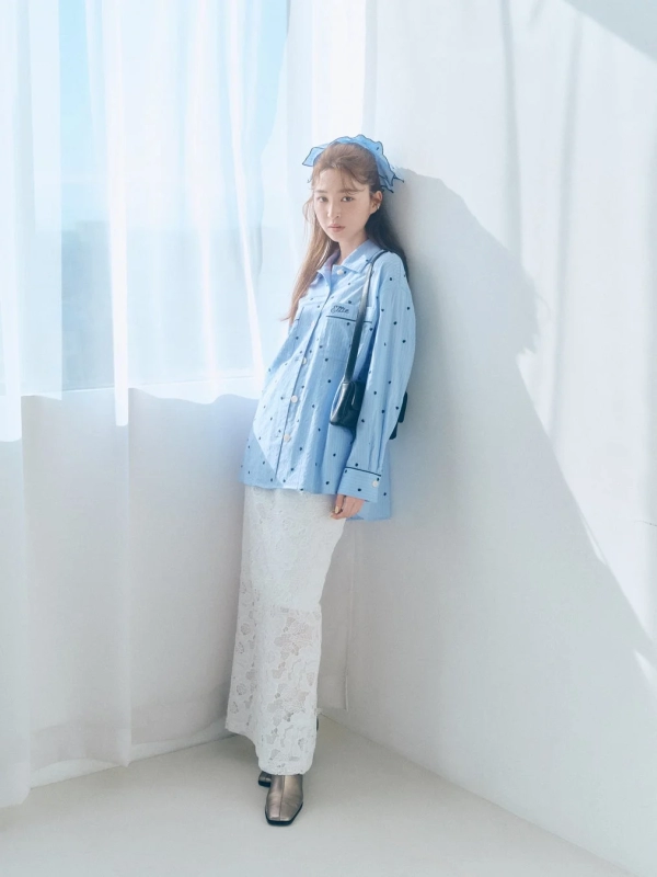 A woman in a light blue polka dot shirt and white lace skirt, with a black bag