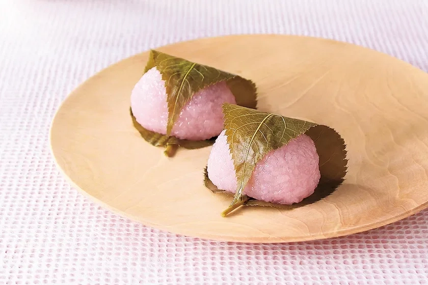 Two sakura mochi on a wooden plate, wrapped in cherry leaves