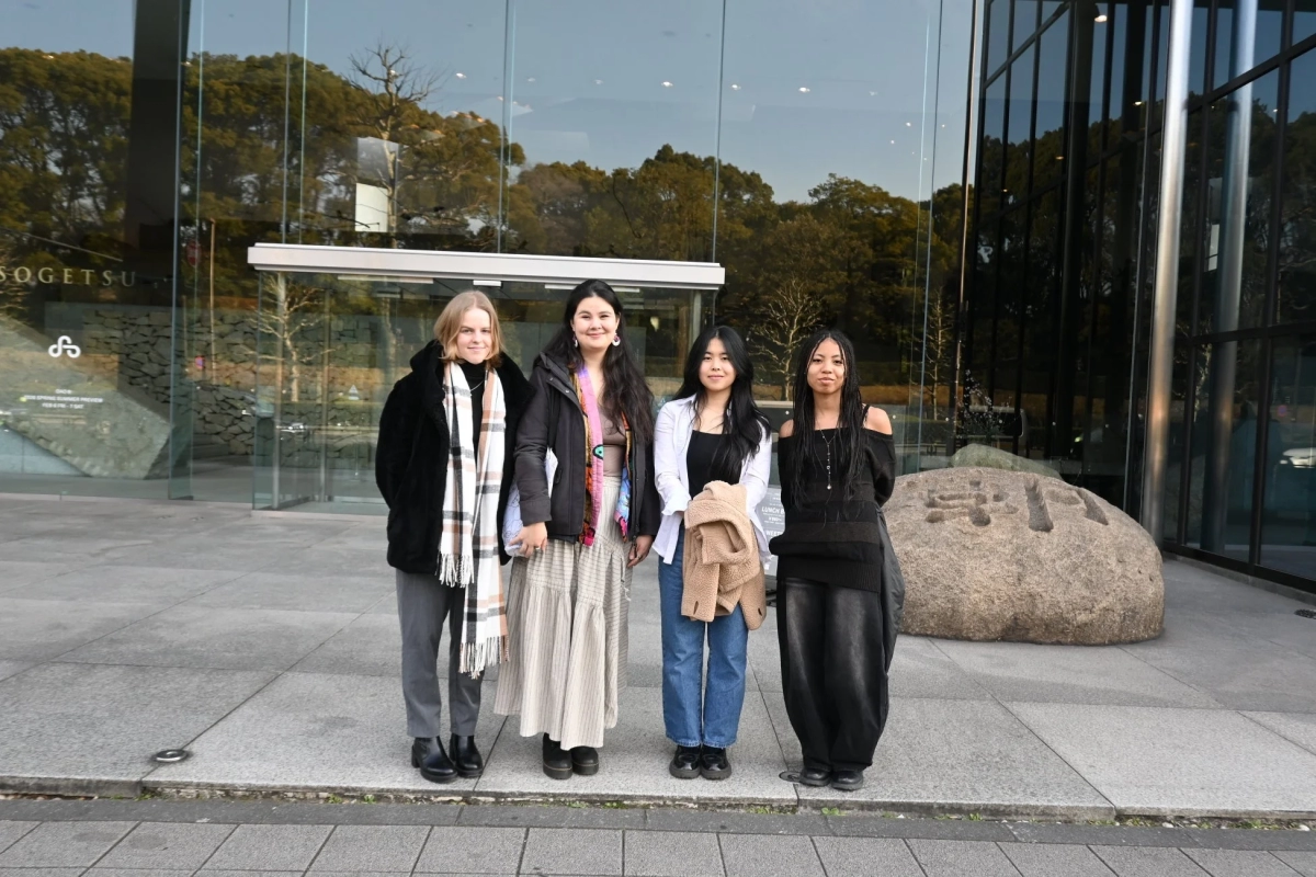 Four young women standing in front of a modern glass building, possibly Minerva University students.